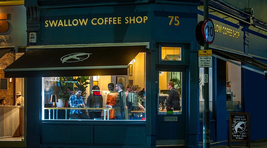 Warmly-lit and inviting corner shopfront of Swallow Coffee Shop, London.